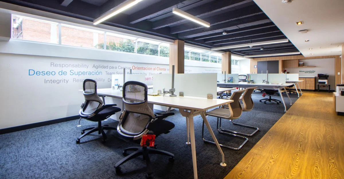 Un espace de bureau moderne et bien éclairé avec des chaises ergonomiques, des tables et des cloisons en verre.