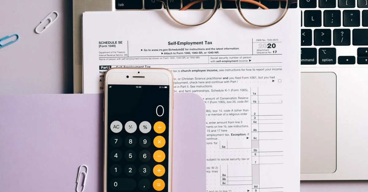 Vue de dessus de documents fiscaux, calculatrice sur smartphone et ordinateur portable pour la comptabilité des travailleurs indépendants.