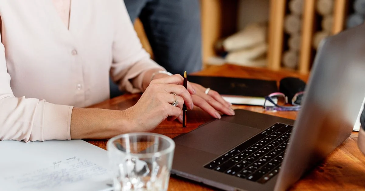 Gros plan sur une femme travaillant sur un ordinateur portable avec des documents sur un bureau. Idéal pour des thèmes professionnels.
