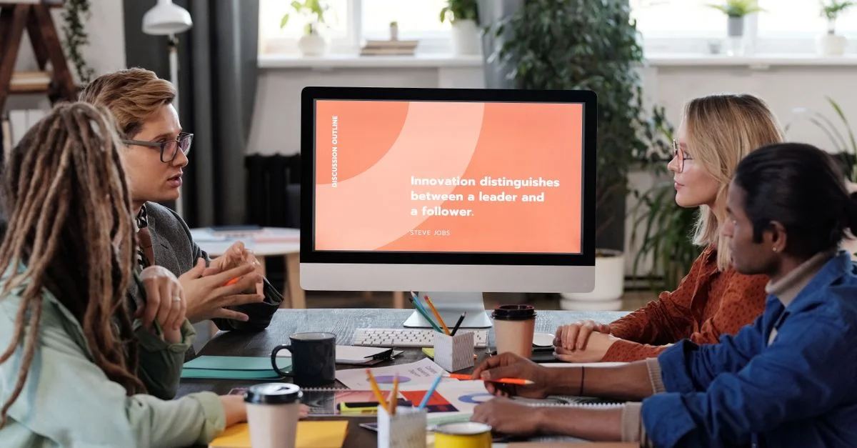 Une équipe multiculturelle collaborant dans un bureau, discutant d'un projet avec un écran visible.