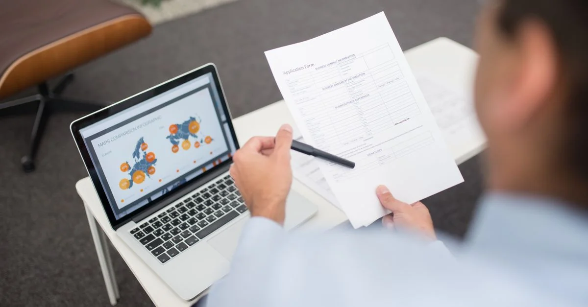 Environnement professionnel avec un homme d'affaires examinant des documents et des données sur un ordinateur portable dans un bureau.