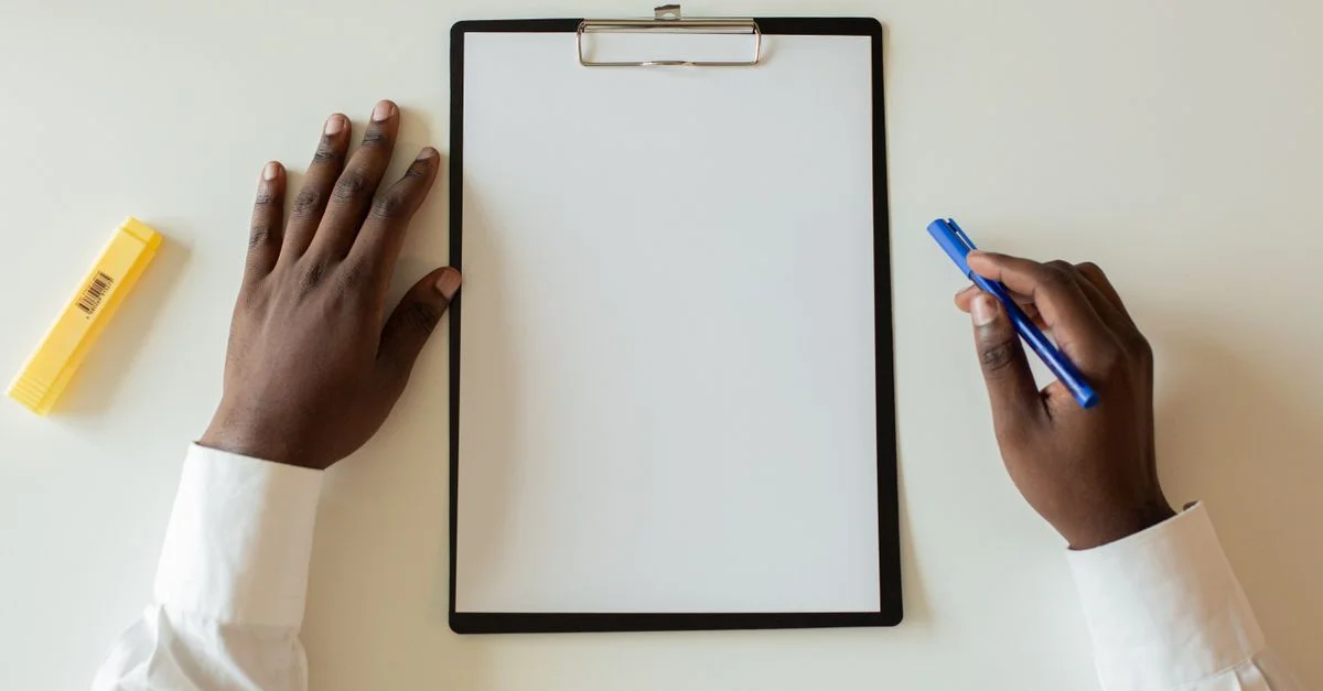 Vue de dessus des mains avec un clipboard blanc et un stylo sur un bureau blanc.