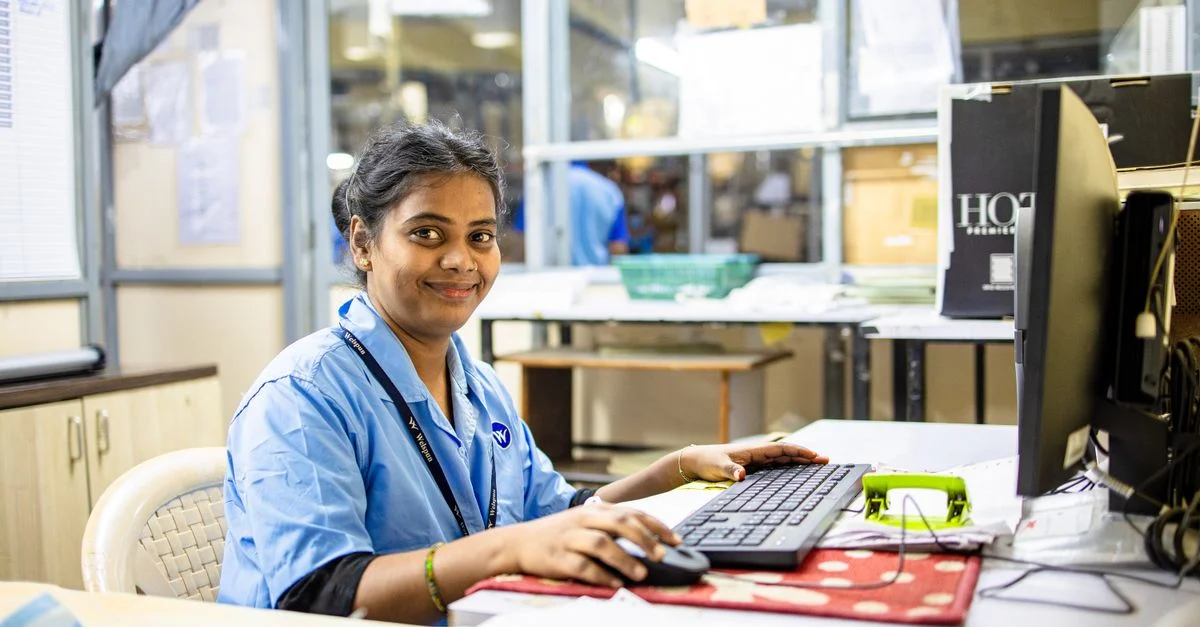 Jeune professionnelle souriante à son bureau dans un environnement de bureau moderne, engagée dans un travail informatique.