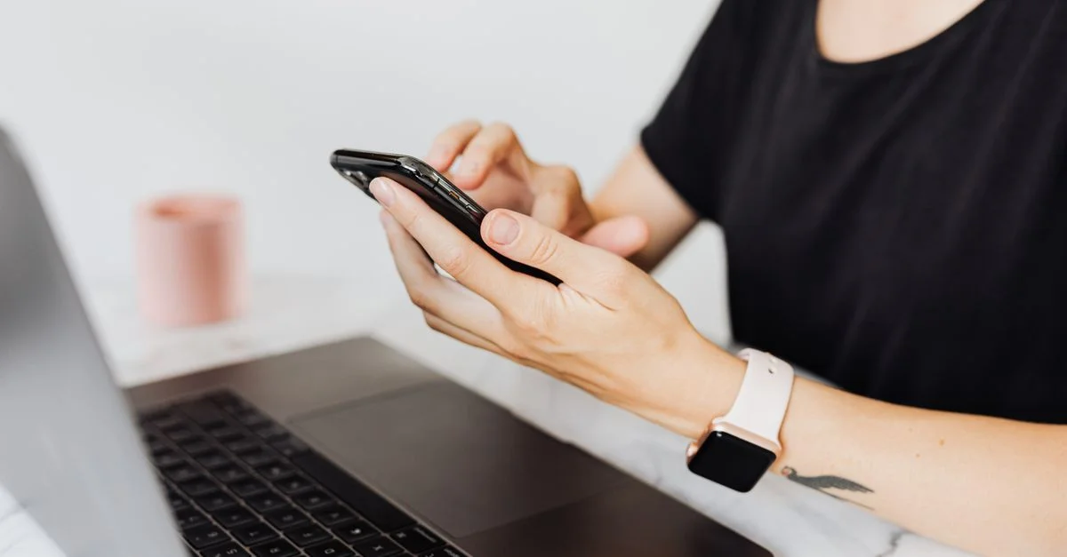 Gros plan sur une femme utilisant un smartphone avec un ordinateur portable sur un bureau de bureau, mettant en valeur la technologie au travail.