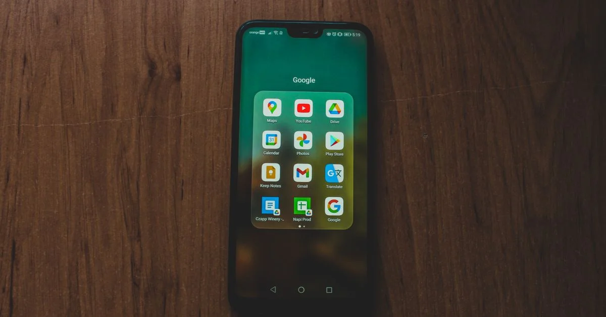 Un smartphone affichant diverses applications Google sur une table en bois.