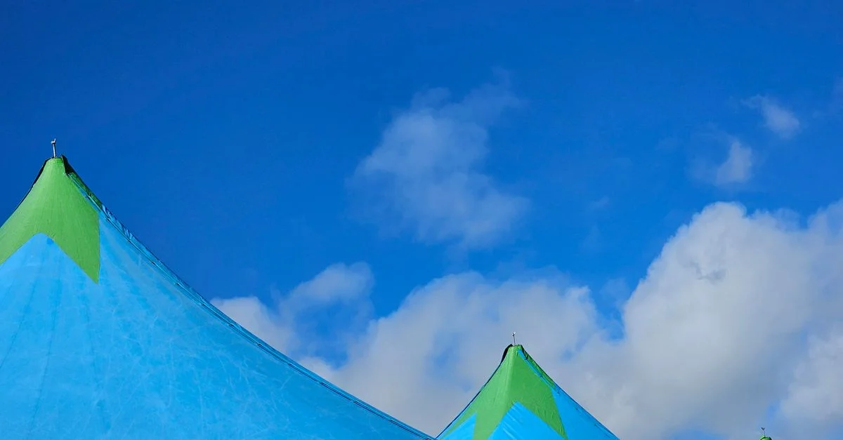 Des tentes bleues vibrantes avec des cimes vertes se détachant sur un ciel lumineux rempli de nuages.