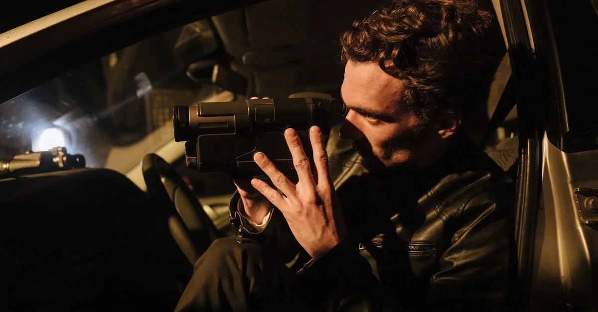 Un homme en veste en cuir utilise un caméscope la nuit dans une voiture.