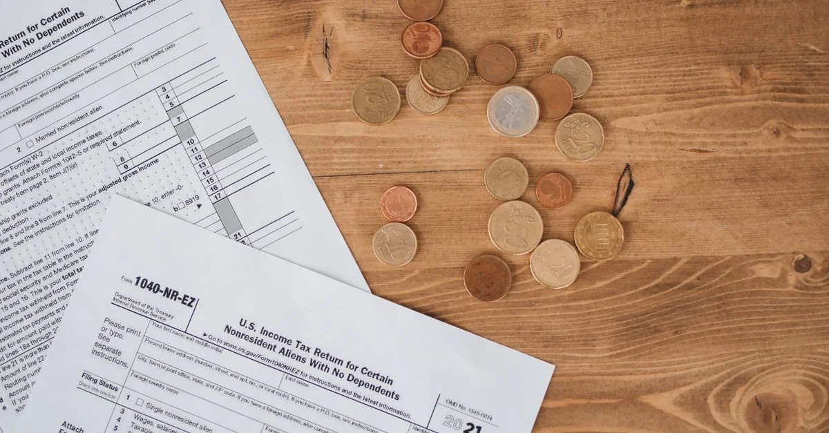 Vue de dessus de formulaires fiscaux et de pièces éparpillées sur une table en bois, illustrant les concepts de finance et de fiscalité.