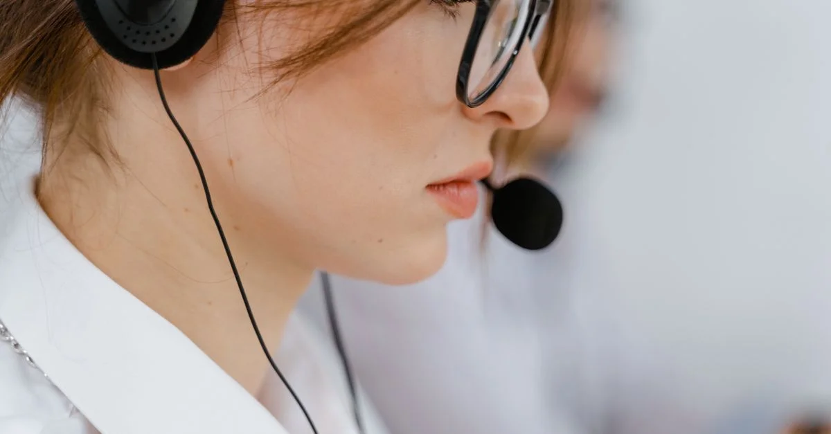 Une jeune femme avec des lunettes et un casque concentrée intensément sur son travail dans un environnement de bureau.