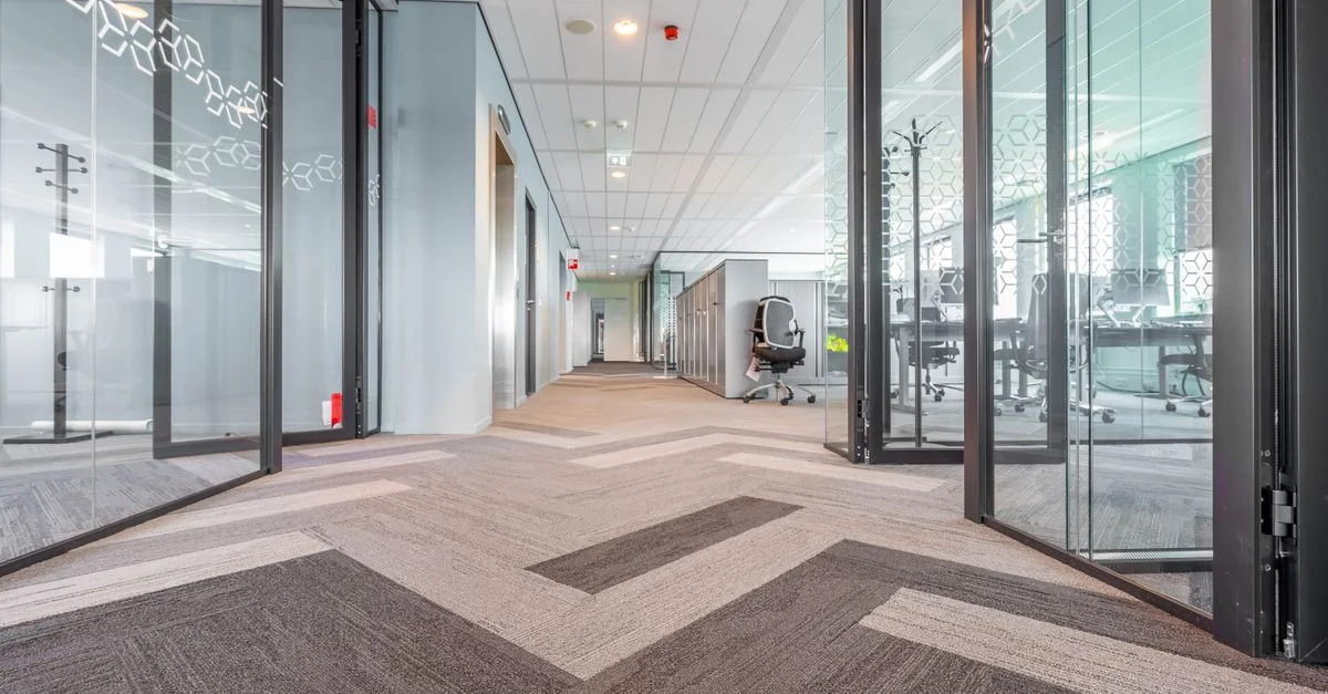 Couloir de bureau moderne, spacieux et lumineux avec des cloisons en verre et un design contemporain.