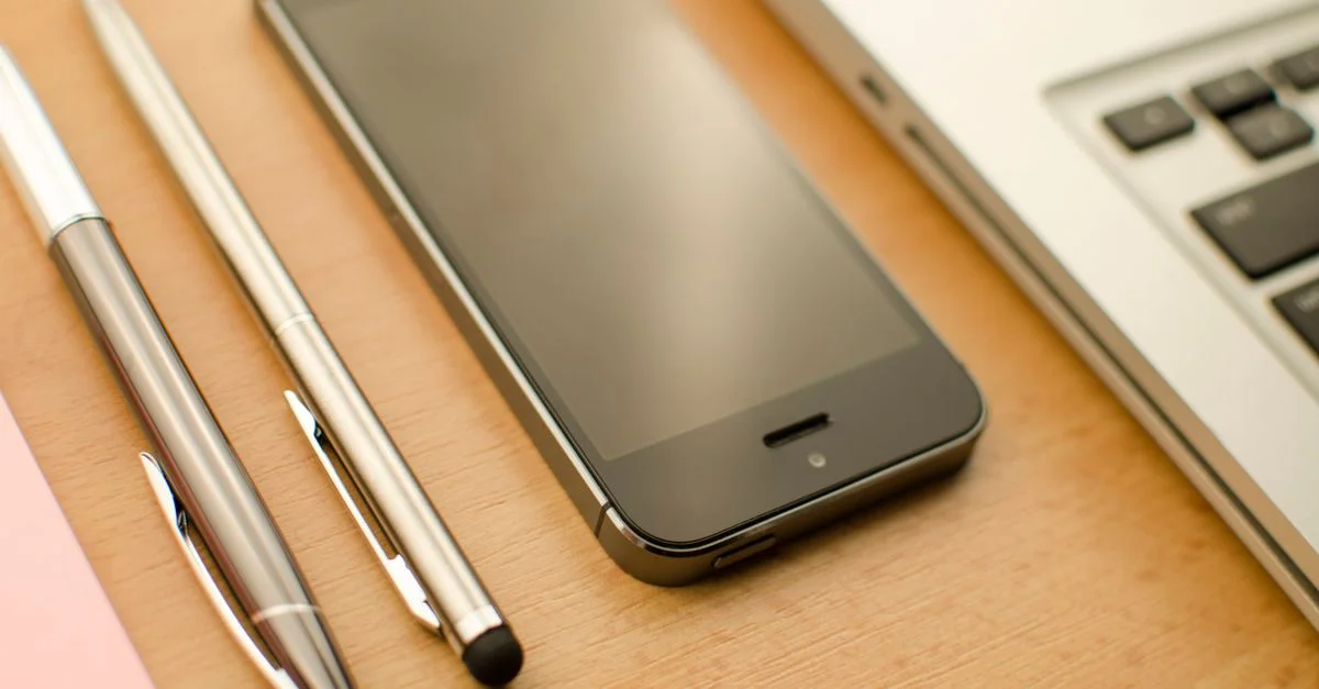 Un bureau bien agencé avec un smartphone, un ordinateur portable et des stylos dans un cadre de bureau.