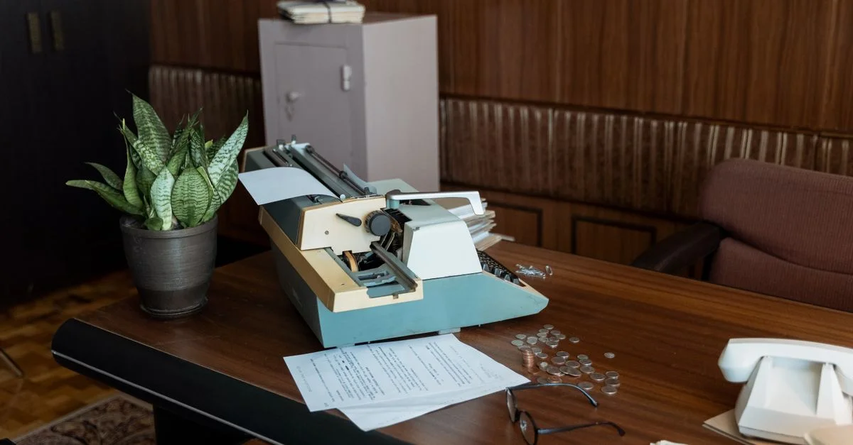 Bureau rétro avec une machine à écrire vintage, des papiers et des pièces sur un bureau en bois.