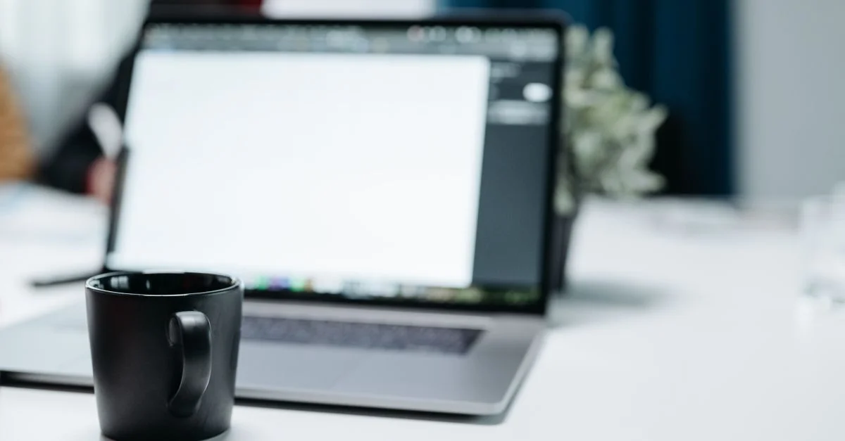 Une tasse de café noire sur un bureau avec un ordinateur portable flou en arrière-plan.