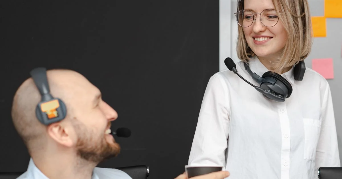 Deux collègues de centre d'appels avec des casques souriant et interagissant dans un environnement de bureau.