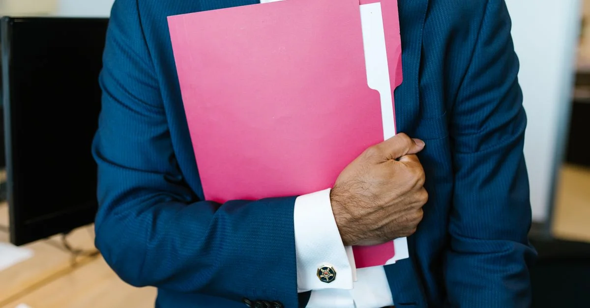 Un homme professionnellement habillé tenant un dossier rose dans un cadre de bureau.