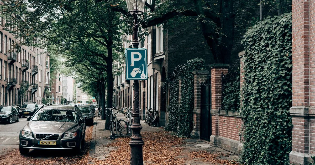 Rue pittoresque de la ville en automne avec des voitures et des vélos alignés le long de trottoirs bordés de feuilles.