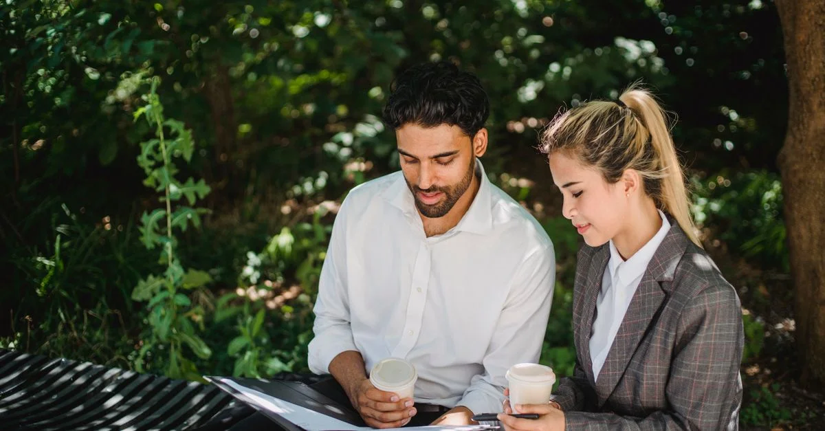 Réunion d'affaires en plein air avec deux professionnels discutant de documents autour d'un café.