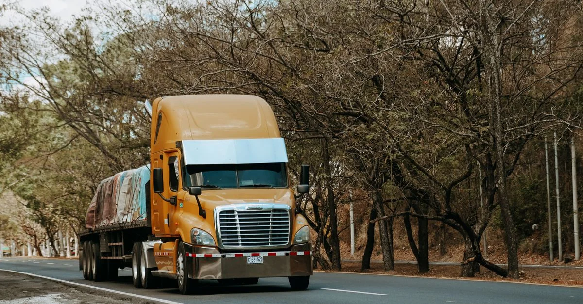 Un camion de marchandises jaune circule sur une route rurale bordée d'arbres, capturant l'essence même du transport au Salvador.