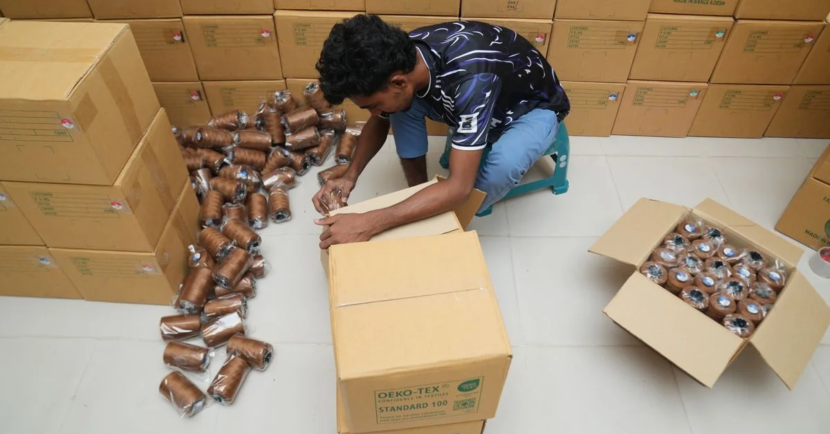 Un homme range des bobines de fil dans un entrepôt rempli de cartons emballés.