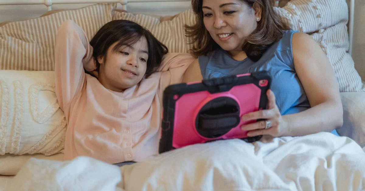 Mère et fille se rapprochant autour d'une tablette dans un cadre domestique chaleureux.
