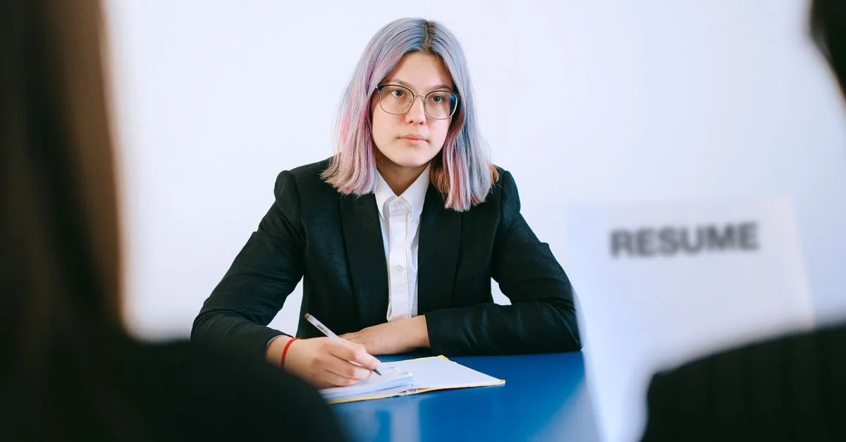 Une jeune femme en costume lors d'un entretien d'embauche, écrivant des notes.