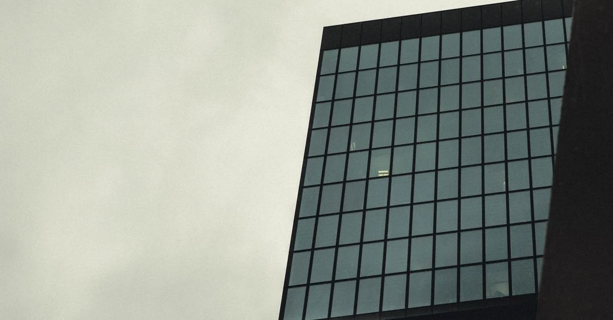 Vue en contre-plongée d'un gratte-ciel moderne avec une façade en verre contre un ciel nuageux.