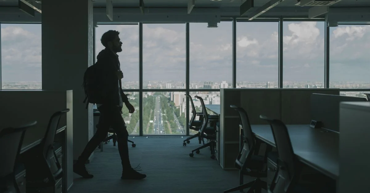 Silhouette d'un homme marchant à travers un intérieur de bureau moderne avec de grandes fenêtres et une vue sur la ville.