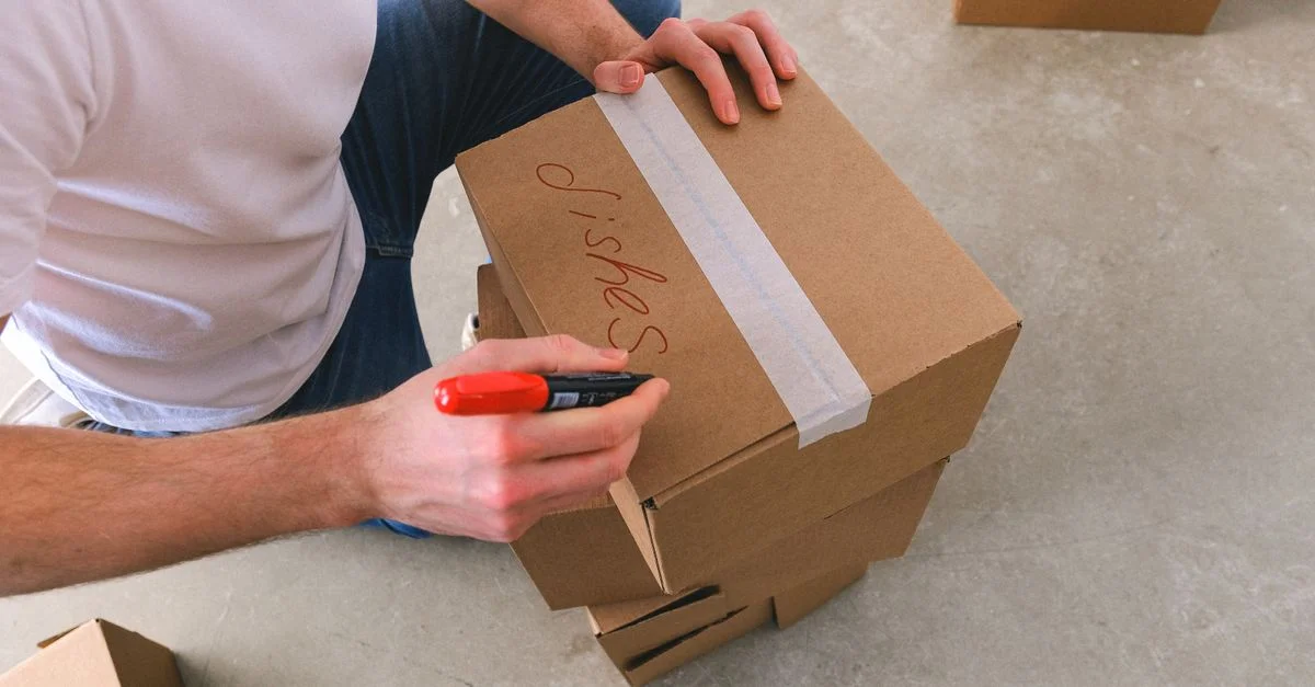 Gros plan d'une personne étiquetant une boîte en carton avec un marqueur rouge, préparant un déménagement.