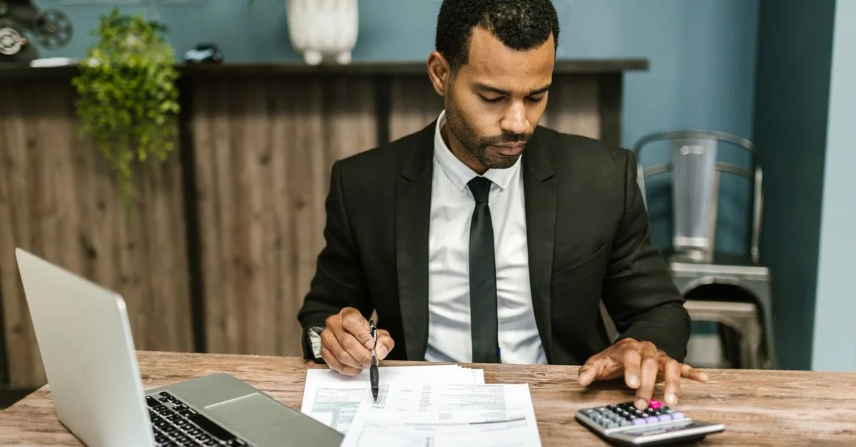 Un homme d'affaires concentré travaille avec une calculatrice et des documents dans un bureau moderne.