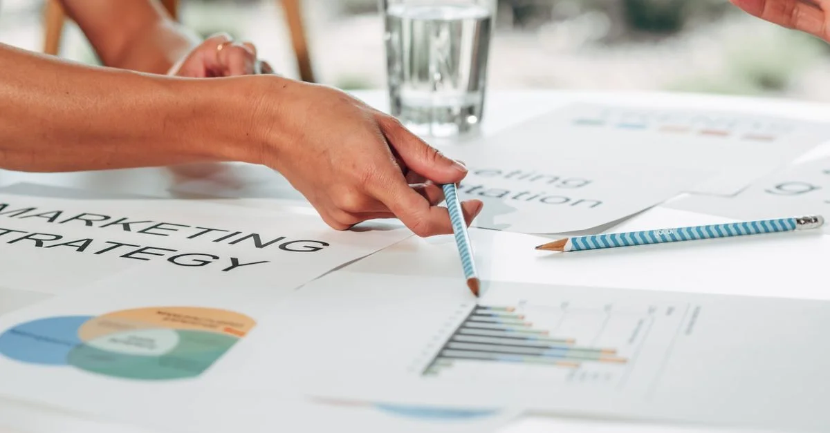 Des mains discutant de la stratégie marketing avec des graphiques dans un cadre de bureau.