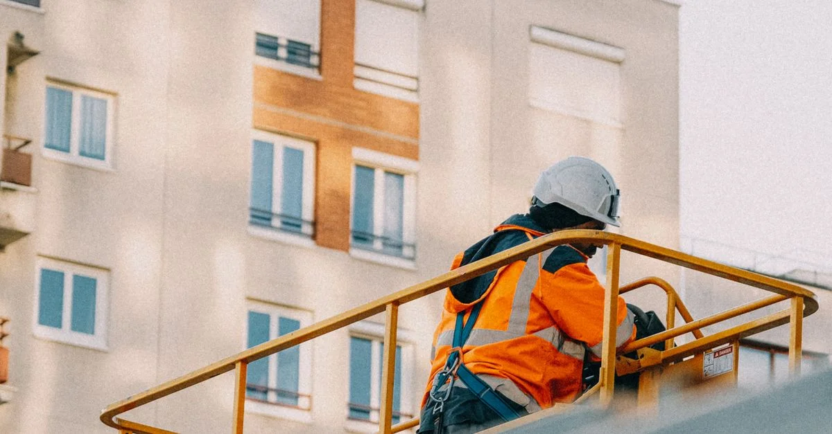 Un ouvrier du bâtiment en équipement de sécurité utilise un élévateur près d'un immeuble résidentiel.