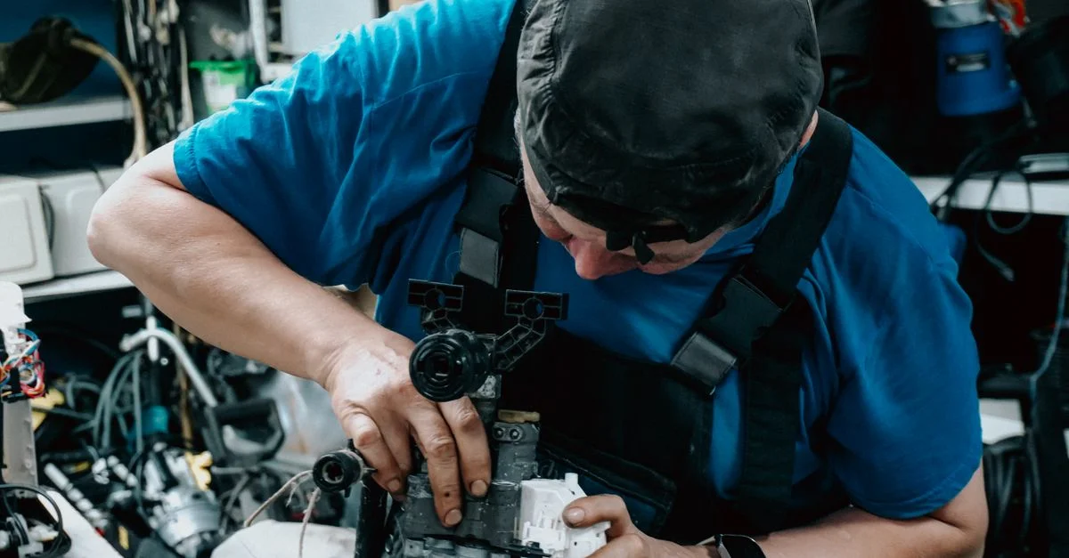 Technicien concentré travaillant sur des machines dans un atelier encombré, faisant preuve d'un savoir-faire exceptionnel.