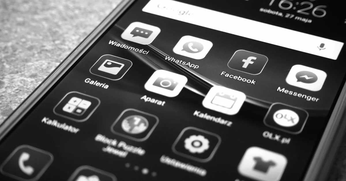 Photo en noir et blanc d'un smartphone affichant des icônes d'applications populaires comme Facebook et WhatsApp.