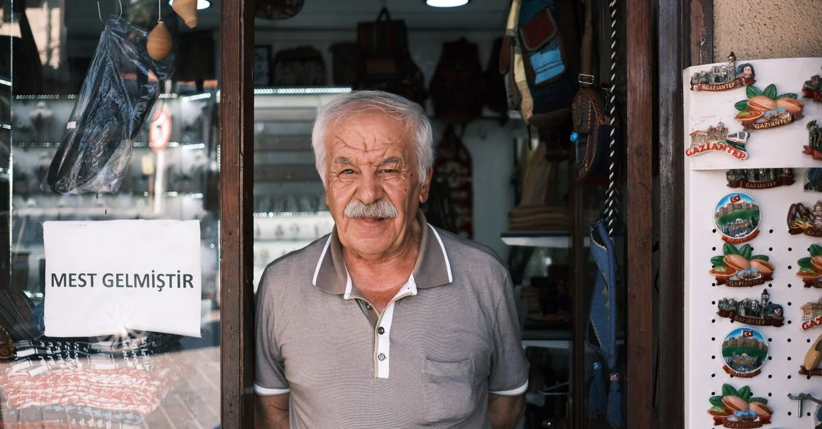 Un vieil homme souriant se tient à l'entrée d'une boutique de souvenirs turcs.