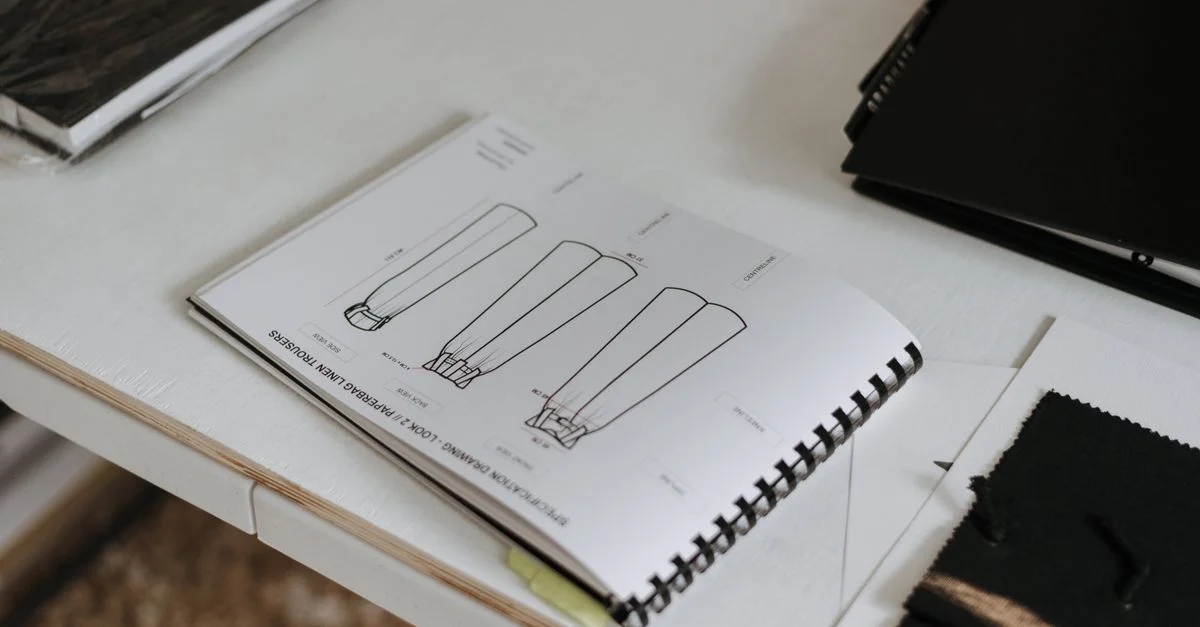 Carnet de croquis de mode ouvert sur le bureau d'un designer, présentant des ébauches de vêtements.