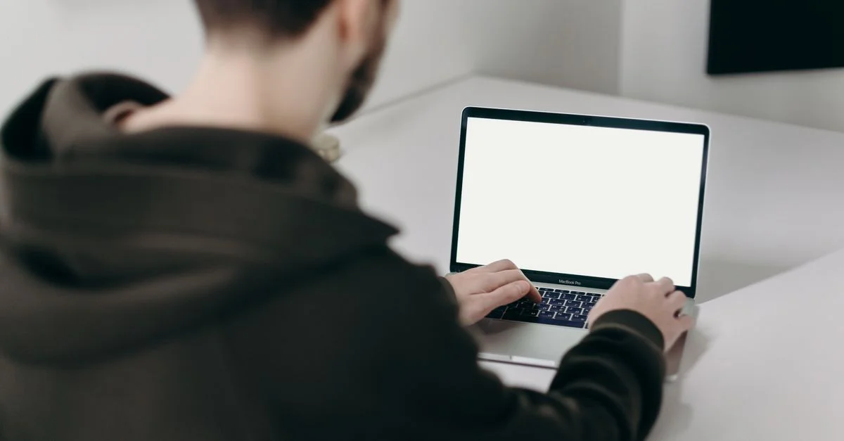 Un jeune homme en sweatshirt travaillant sur un ordinateur portable avec un écran vide dans un bureau minimaliste à domicile.