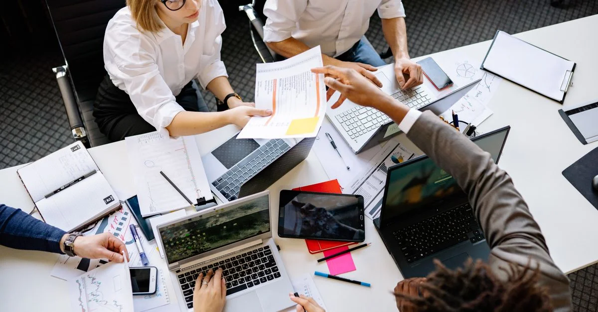 Équipe diversifiée collaborant dans un bureau moderne avec des ordinateurs portables et des documents.