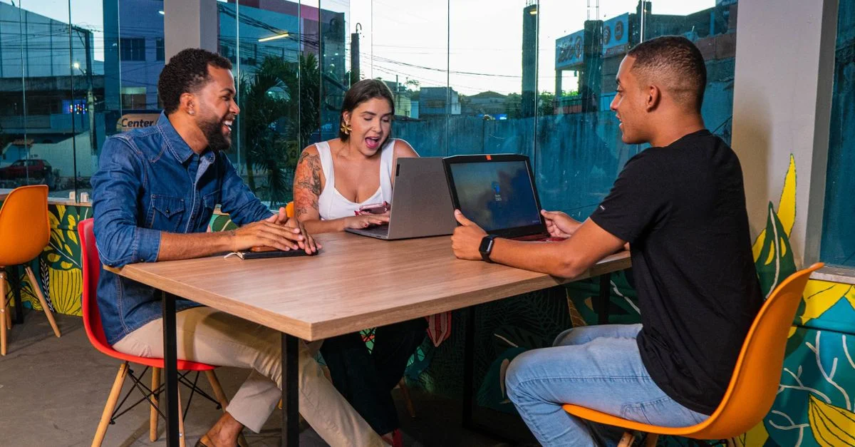 Trois collègues assis à une table travaillant sur des ordinateurs portables dans un espace de bureau urbain dynamique.