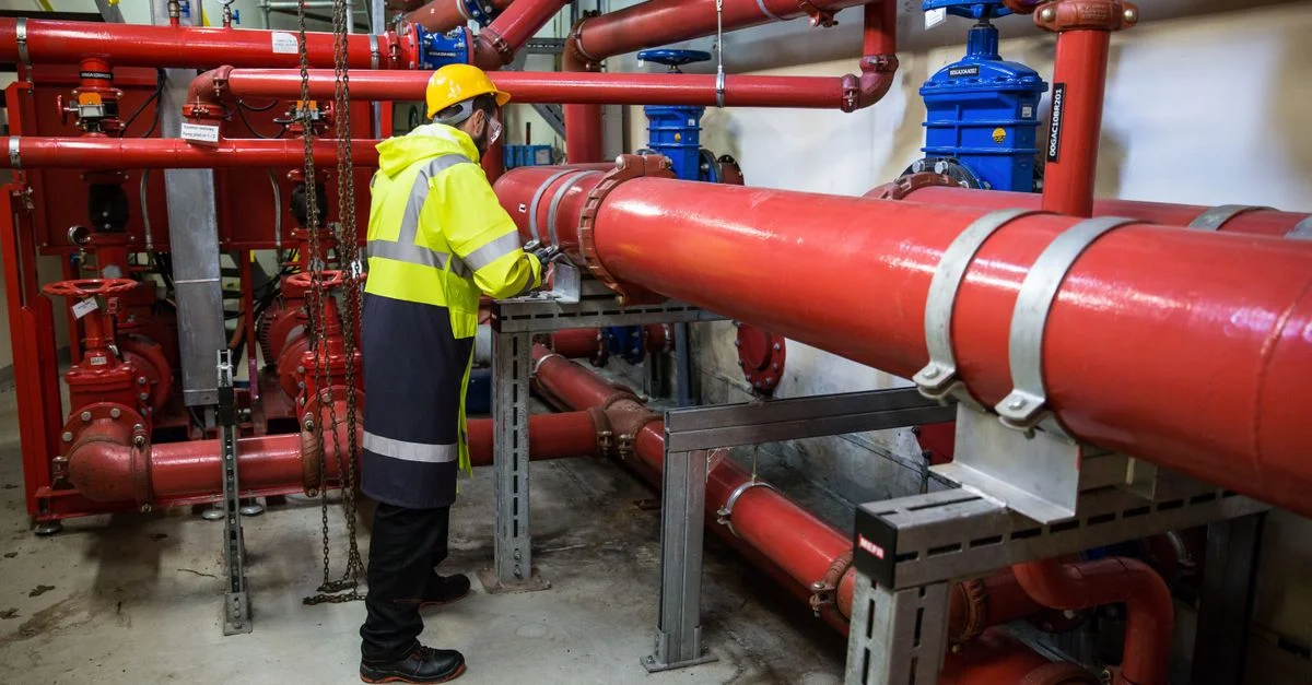 Ingénieur avec équipement de sécurité inspectant un système de tuyauterie industrielle rouge à l'intérieur.