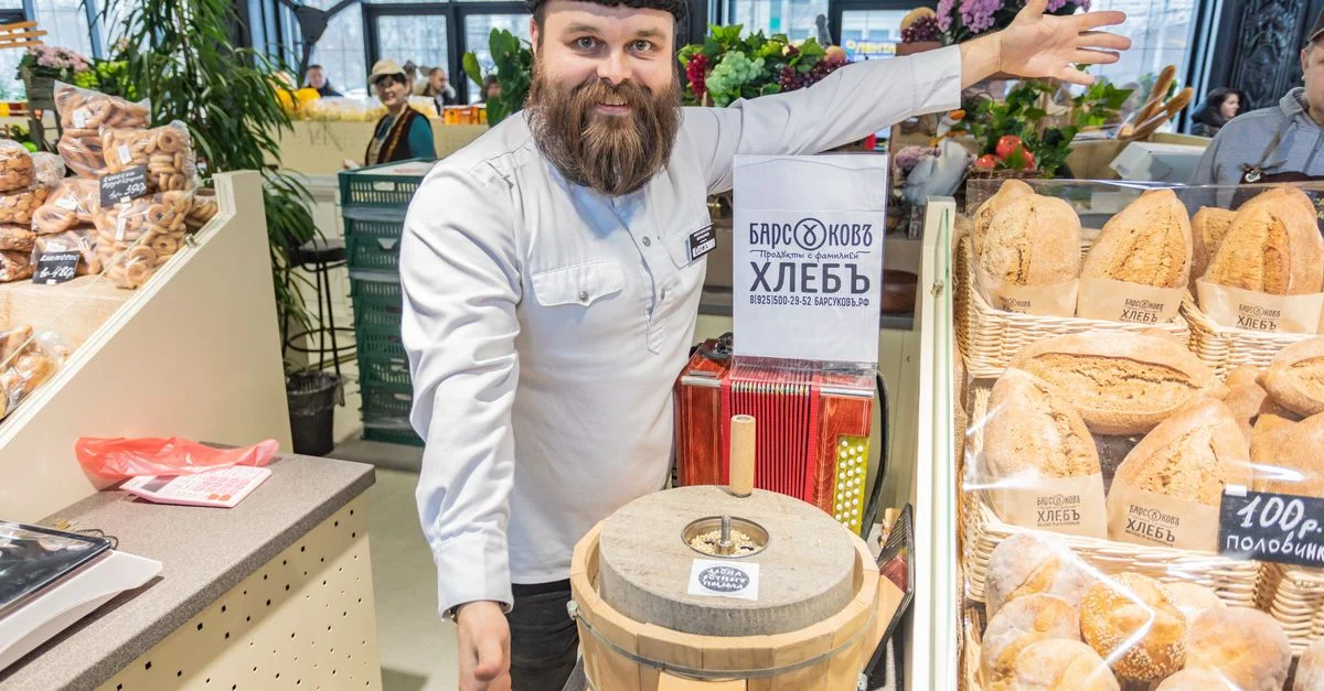 Boulanger joyeux présentant du pain fraîchement cuit dans une boulangerie de Moscou, mettant en avant des ingrédients naturels et des méthodes traditionnelles.