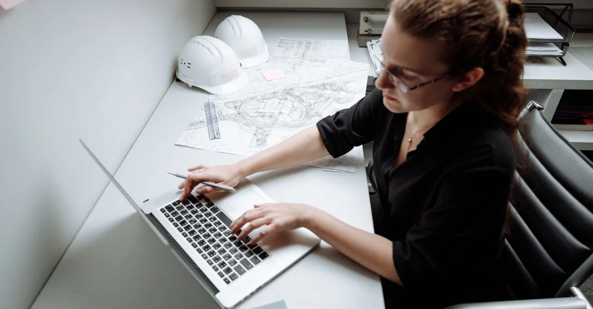 Femme architecte travaillant sur un ordinateur portable à son bureau avec des plans et des casque de sécurité.