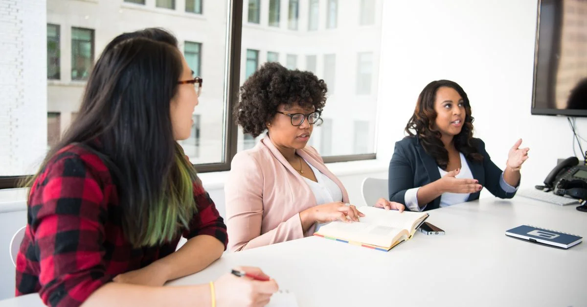 Trois femmes participent à une réunion professionnelle dans un bureau moderne.