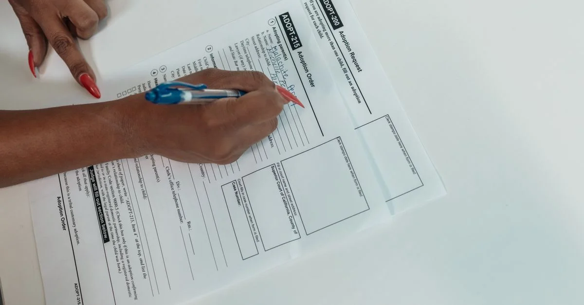Gros plan d'une main remplissant un formulaire de demande d'adoption avec un stylo.