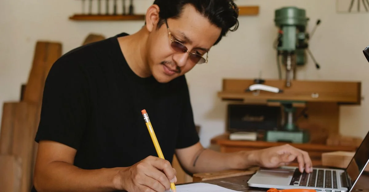Un artisan esquisse avec diligence un design tout en utilisant un ordinateur portable dans son atelier de travail du bois.