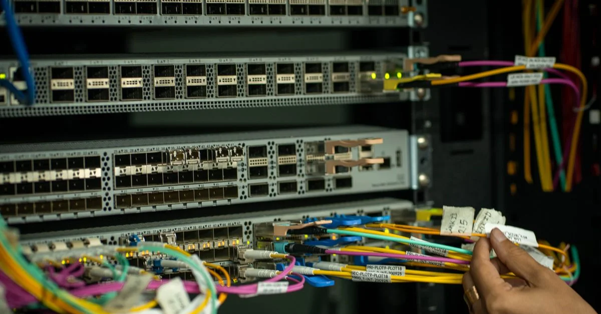 Une main manipulant des câbles à fibres optiques dans une salle serveur, illustrant la connectivité moderne.