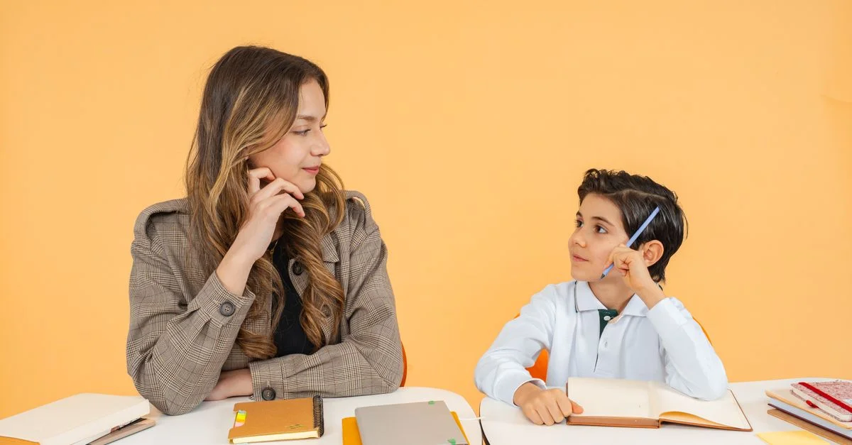 Un enseignant et un élève ayant une discussion attentive dans un cadre de classe avec des carnets et des stylos.