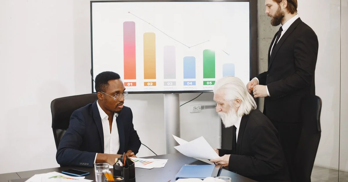 Trois hommes d'affaires discutant de données financières dans un bureau moderne avec des graphiques.