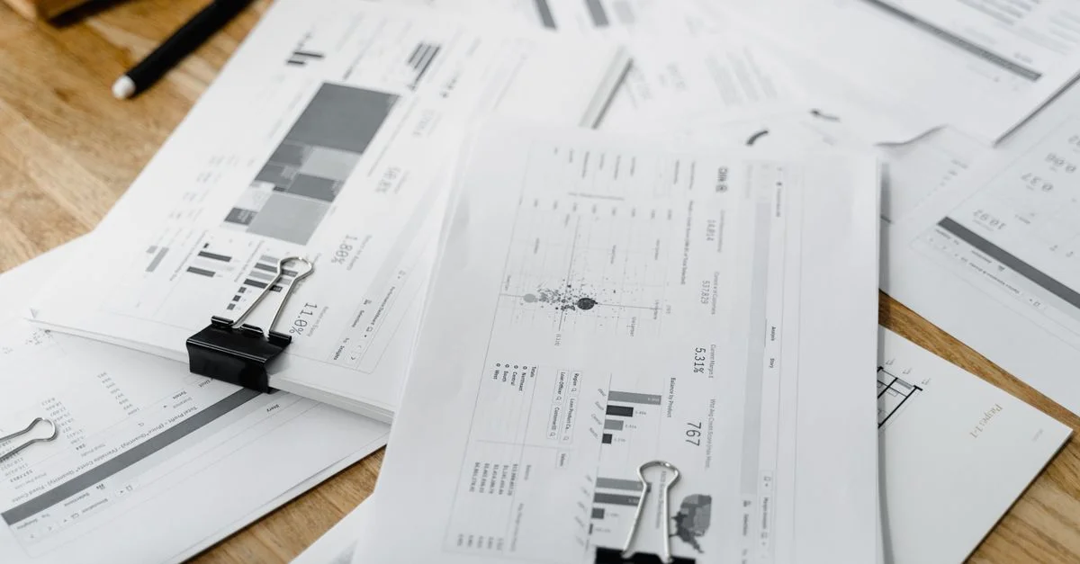 Une pile de rapports financiers et de graphiques avec des agrafes sur un bureau en bois, mettant en avant la planification d'entreprise.
