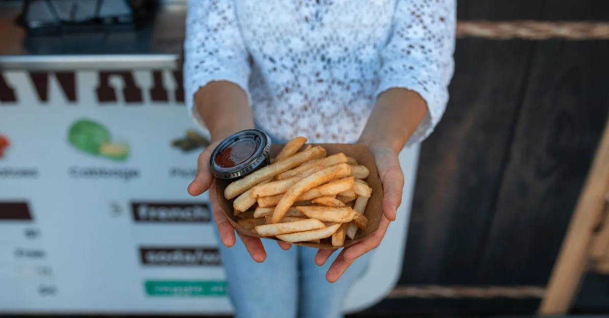 Une personne tient une portion de frites croustillantes avec du ketchup devant un stand de nourriture.