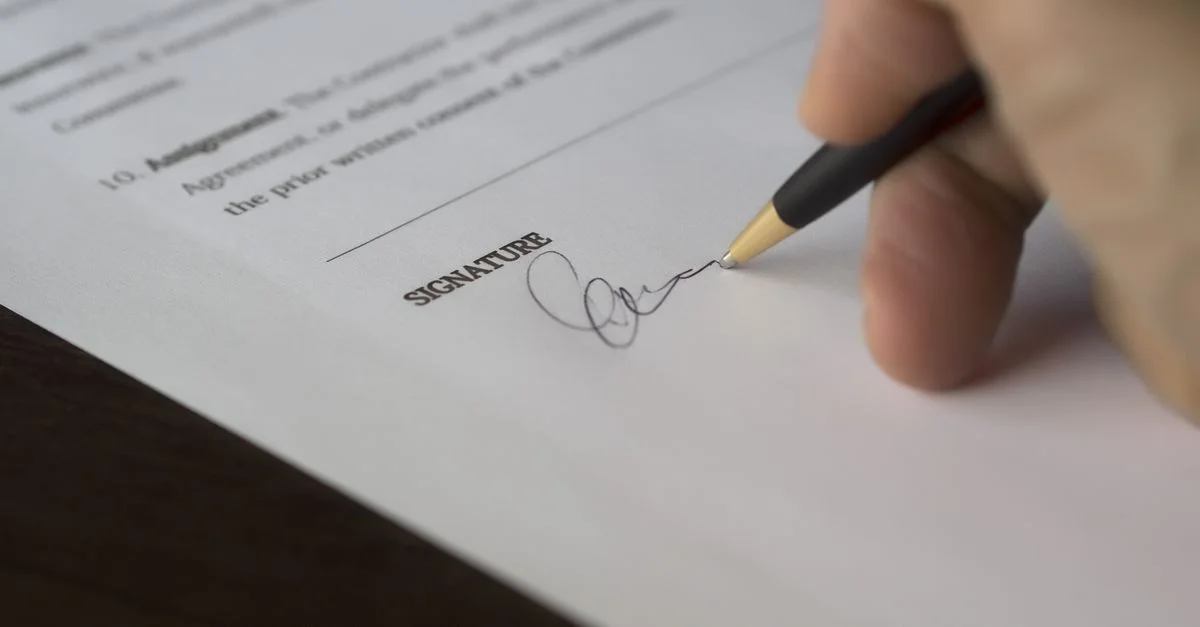 Une main signe un contrat formel avec un stylo sur un bureau en bois.